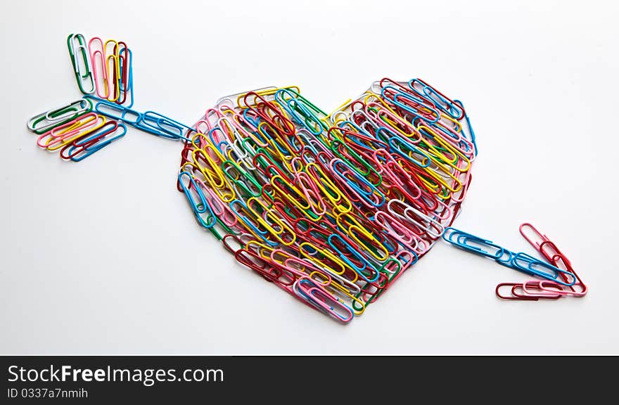 Multi coloured paper clips arraged in heart shape strucked with arrow on isolated white background. Multi coloured paper clips arraged in heart shape strucked with arrow on isolated white background.