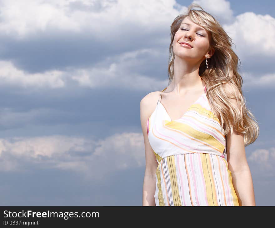 Outdoor portrait of a young lady on a blue cloudy sky background. Outdoor portrait of a young lady on a blue cloudy sky background