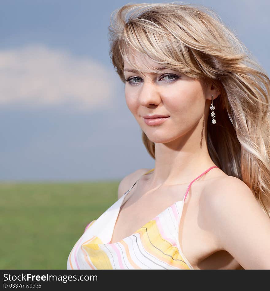 Outdoor portrait of a young lady on a blue cloudy sky background. Outdoor portrait of a young lady on a blue cloudy sky background