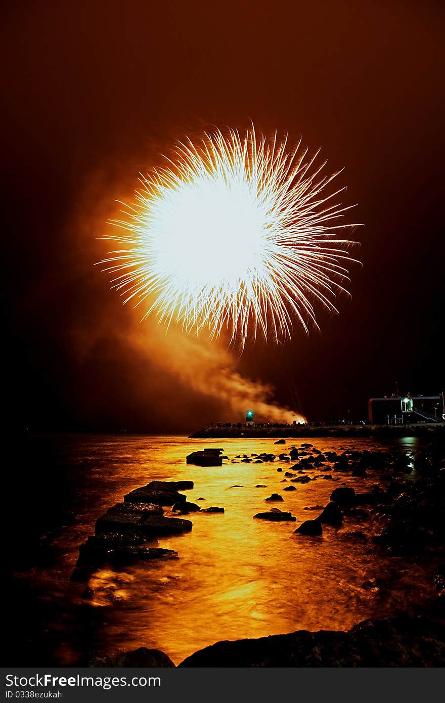 Orange fireworks launched at the shoreline of the harbor