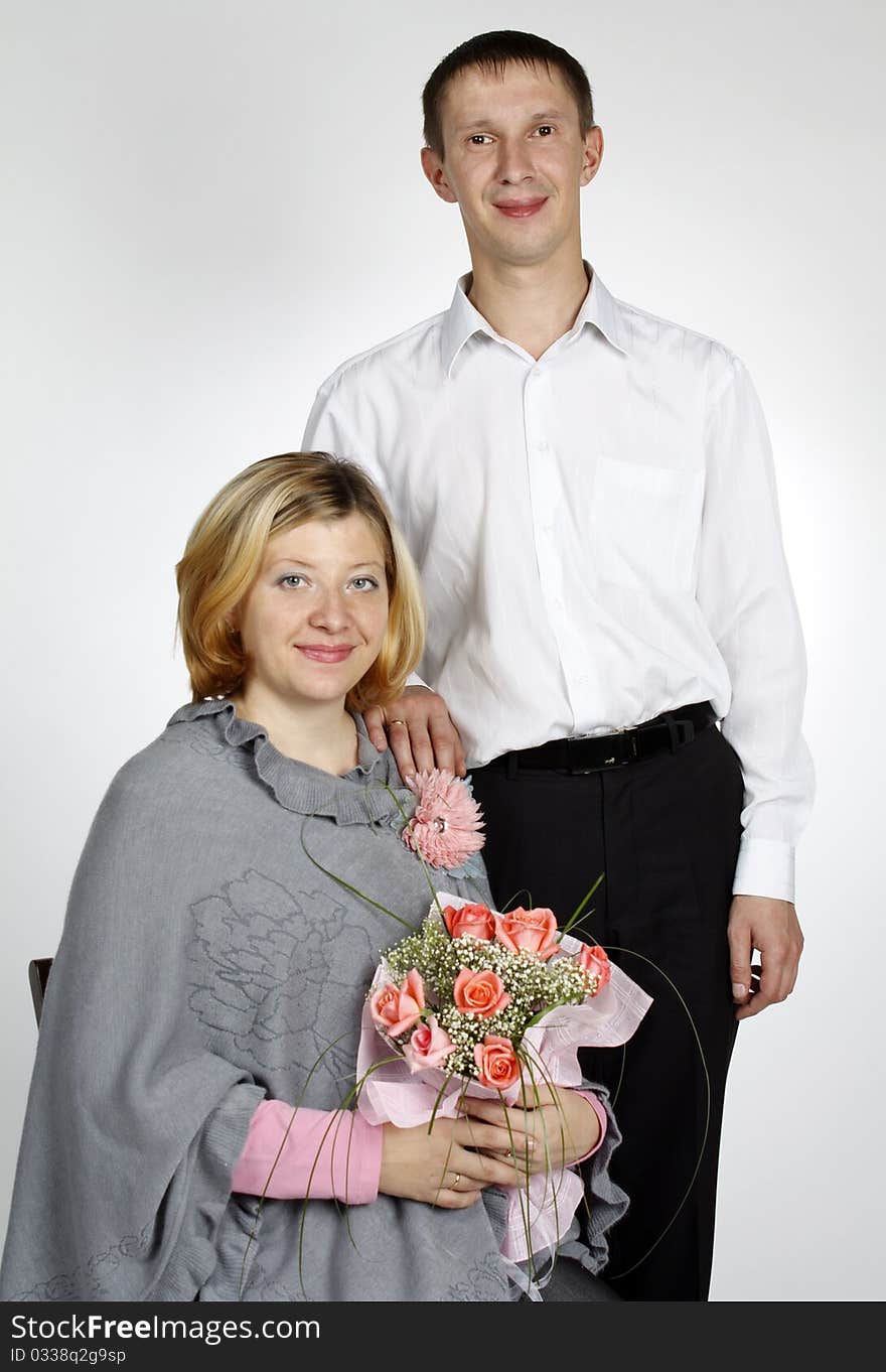 The pregnant woman sits on a chair, holds a bouquet, the man costs near to it having put a hand on a shoulder. The pregnant woman sits on a chair, holds a bouquet, the man costs near to it having put a hand on a shoulder