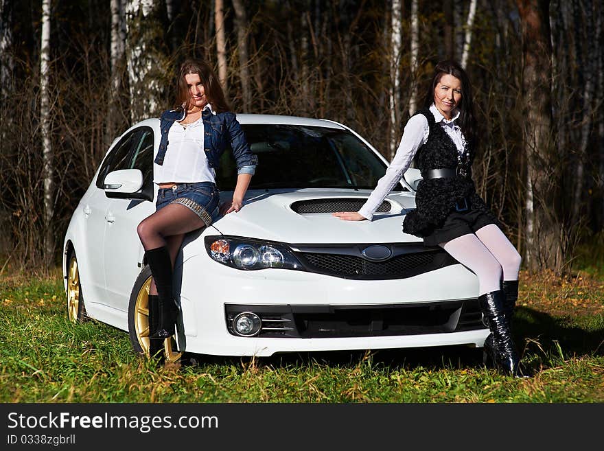 Two beautiful girls friend on the background of the stylish white sports car. Two beautiful girls friend on the background of the stylish white sports car