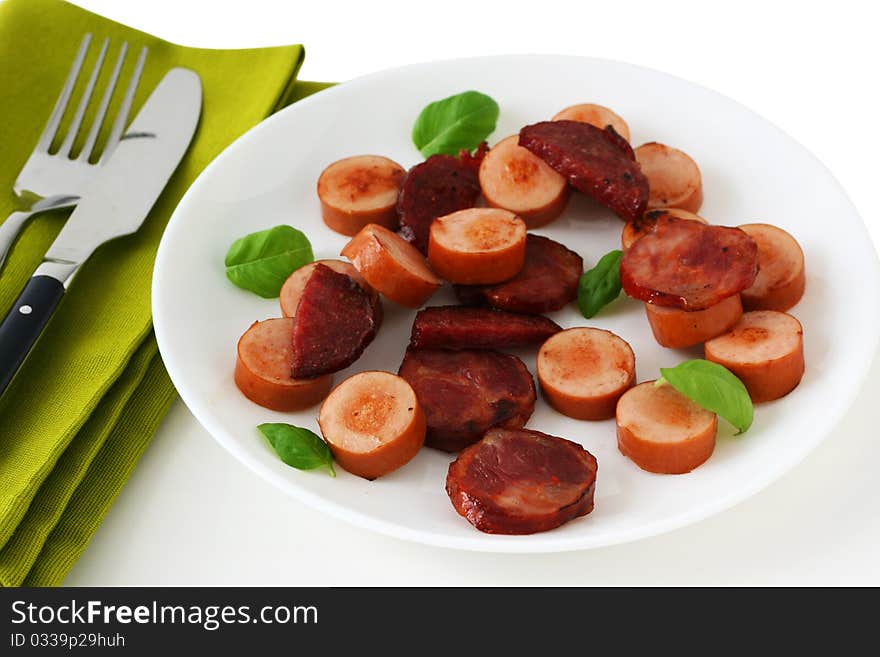 Fried sausages with basil on an white plate