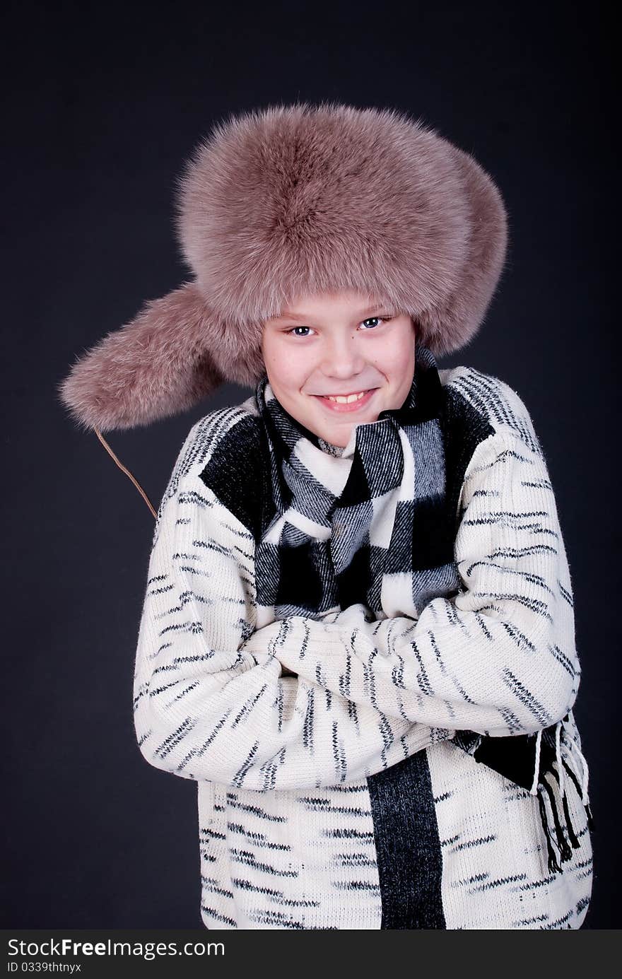 Portrait of a cheerful boy in winter hat on a dark studio background