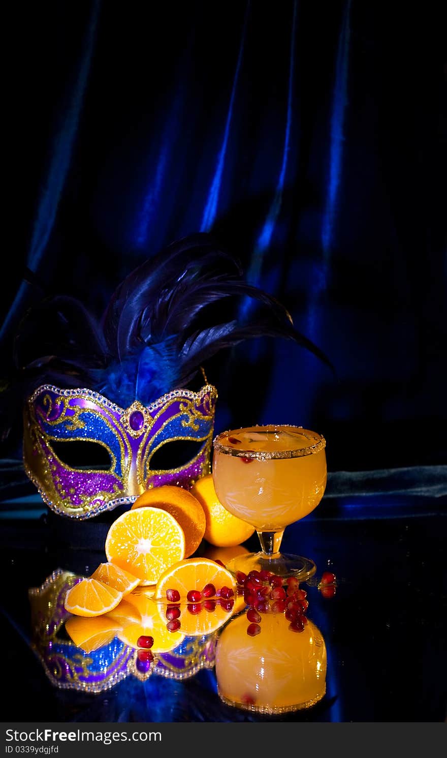 Drink in a glass, tangerines, grains of a pomegranate and a mask on a dark blue background. Drink in a glass, tangerines, grains of a pomegranate and a mask on a dark blue background