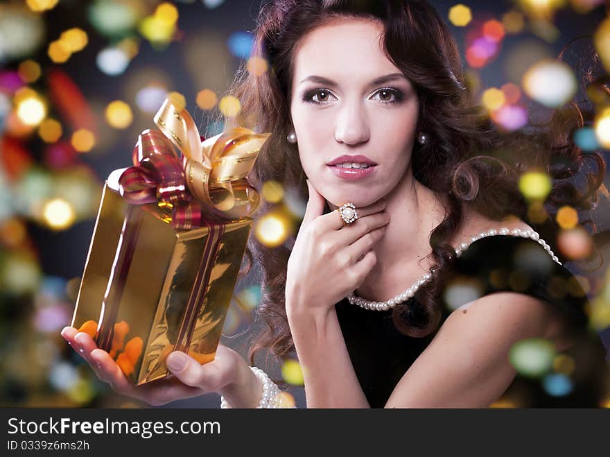 A cute young girl holding a christmas gift,dark background with christmas light bokeh. A cute young girl holding a christmas gift,dark background with christmas light bokeh