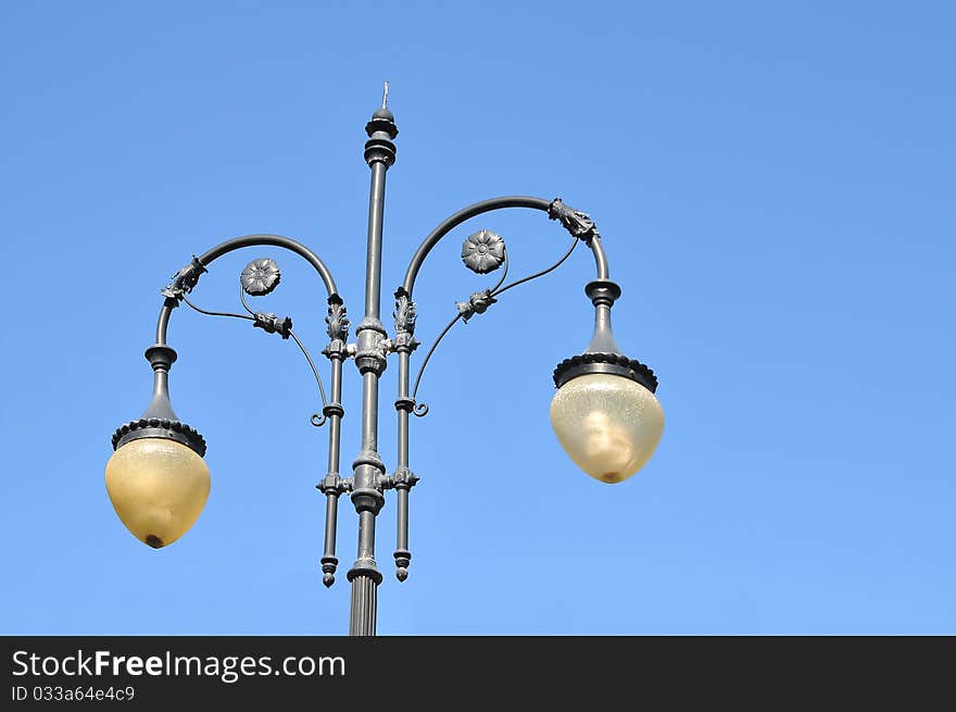 A photo of an old street lamppost against a blue sky. A photo of an old street lamppost against a blue sky.