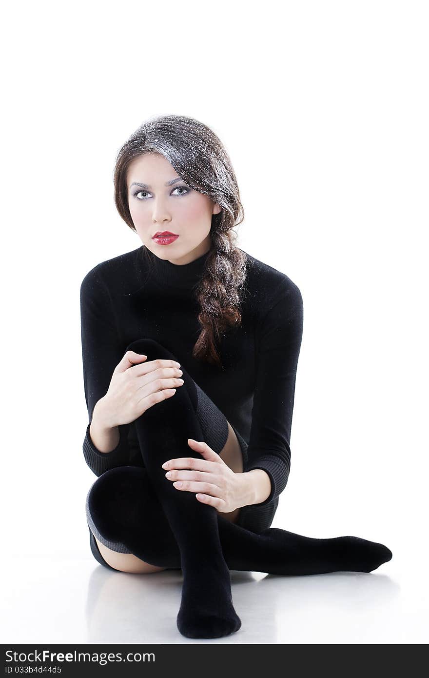 Fashion model wearing winter clothes with snow on her hair posing in studio