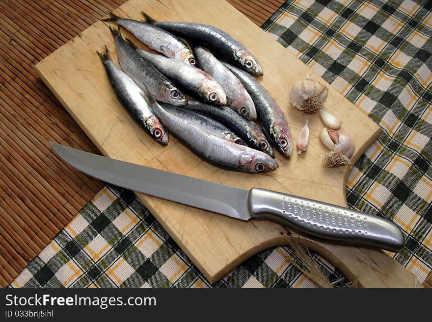 Fresh sardine on cutting board with knife and garlic by side. Fresh sardine on cutting board with knife and garlic by side