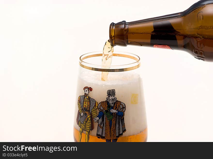 Light foamy beer is poured out of the bottle in glass on a white background