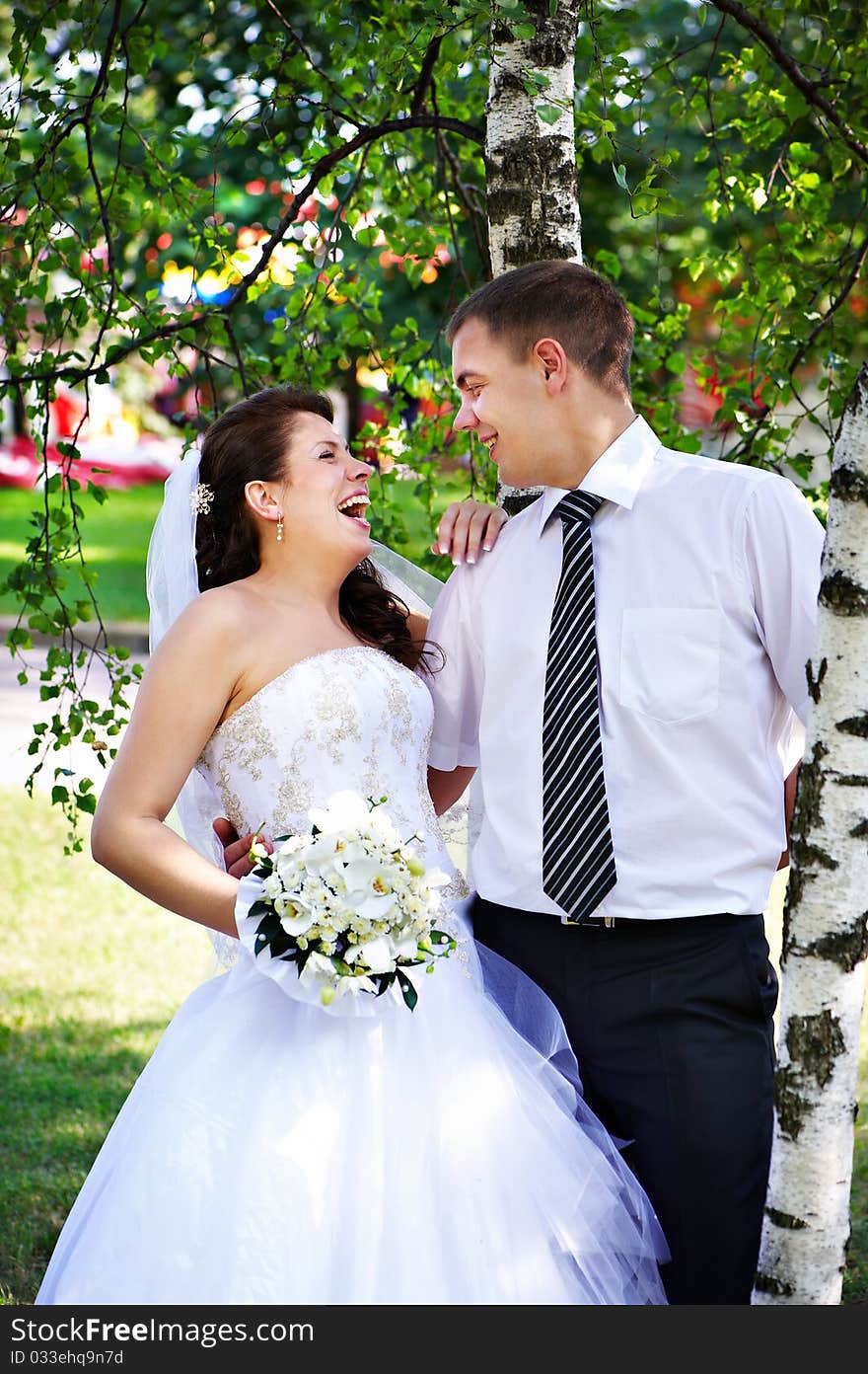 Joyful bride and groom near birches on grass in park