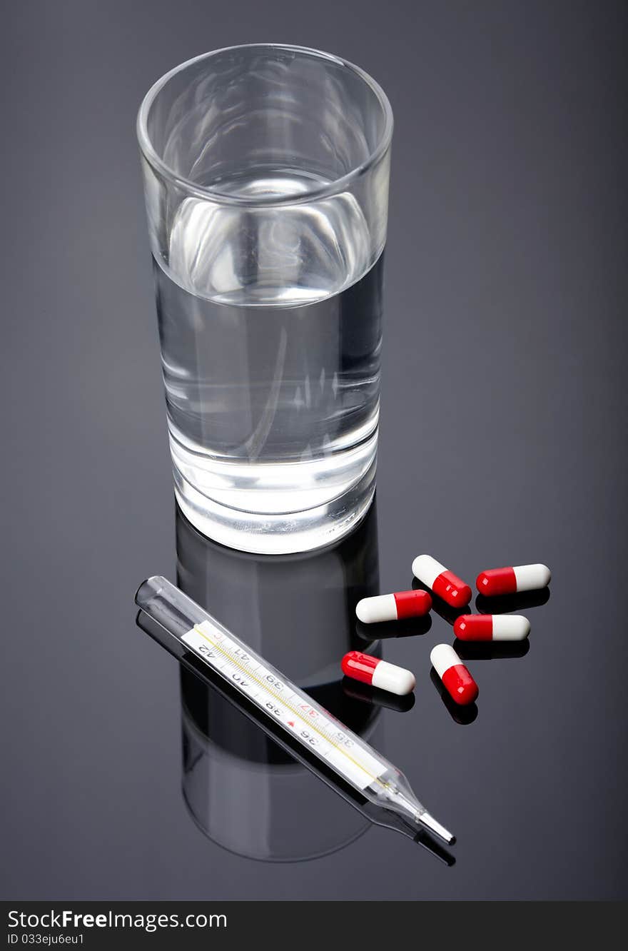 Pills, thermometer and glass of water over dark background