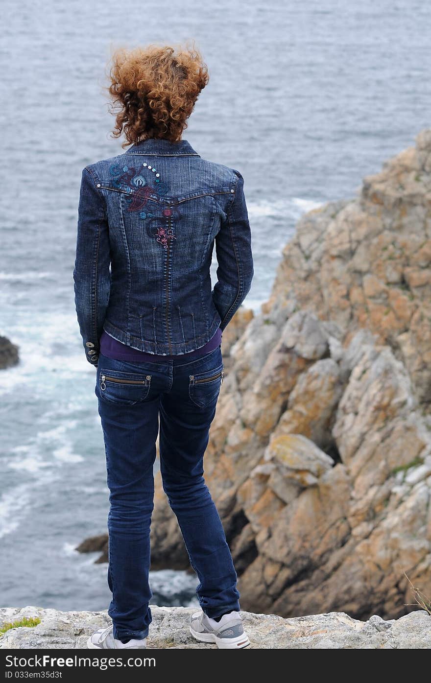 Young curly woman watching the coast and ocean of brittany, france. Young curly woman watching the coast and ocean of brittany, france.