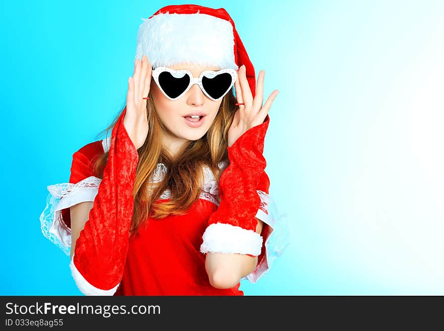 Beautiful young woman in Santa Claus clothes over blue background. Beautiful young woman in Santa Claus clothes over blue background.