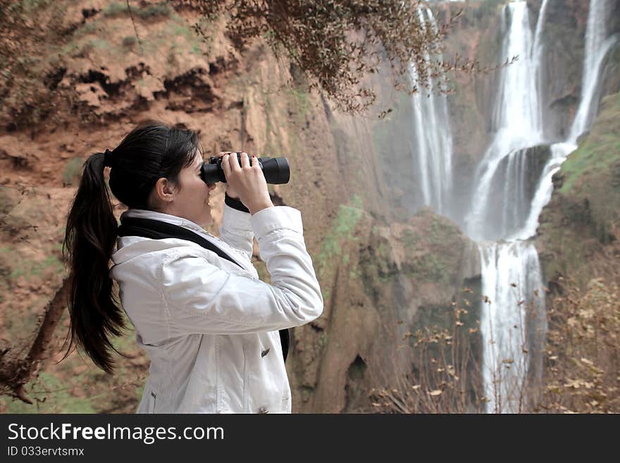 Young woman observing Ouzoud waterfalls with binoculars. Young woman observing Ouzoud waterfalls with binoculars