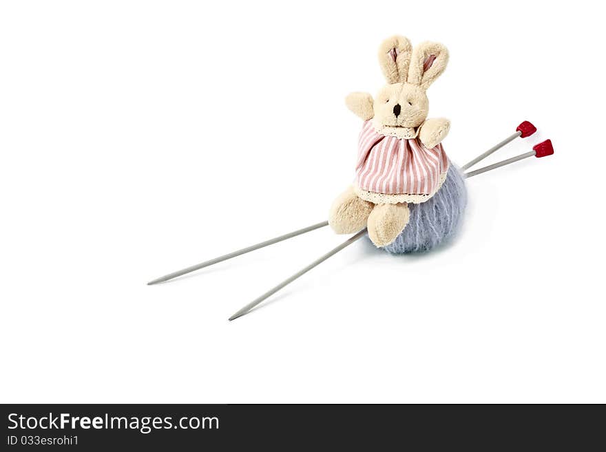 Toy little doe rabbit sitting on grey woolen mohair clew with knitting needles isolated on white background. Toy little doe rabbit sitting on grey woolen mohair clew with knitting needles isolated on white background