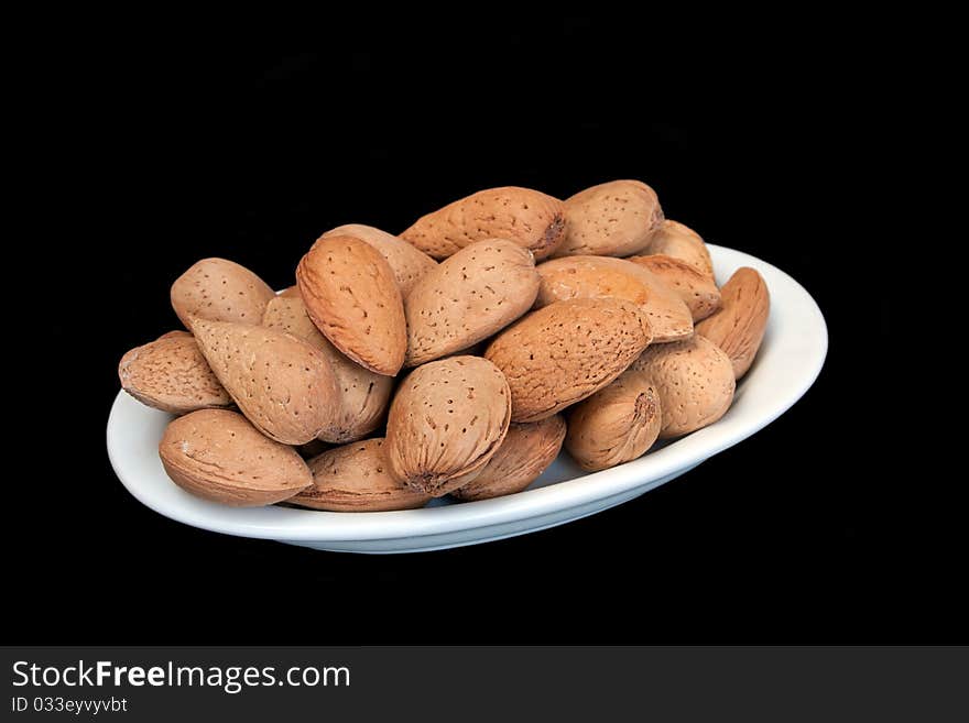 Almonds in nutshell on small oval plate in isolated over black