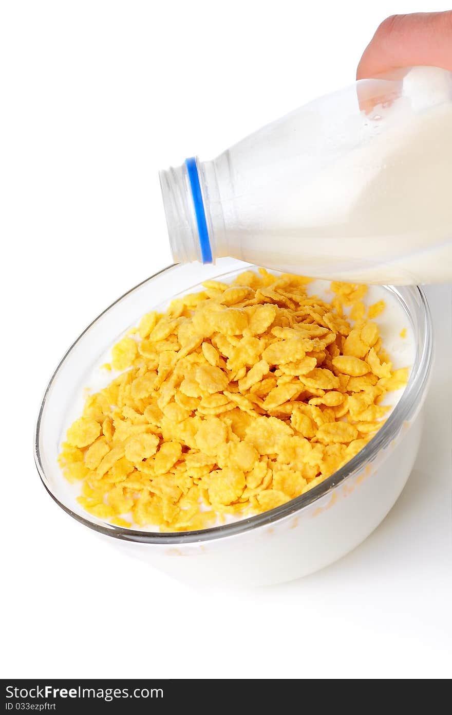 Granola with milk in glass bowl and spoon on white surface.