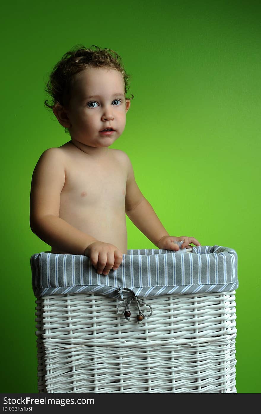 Baby sitting in a basket over a green background wall