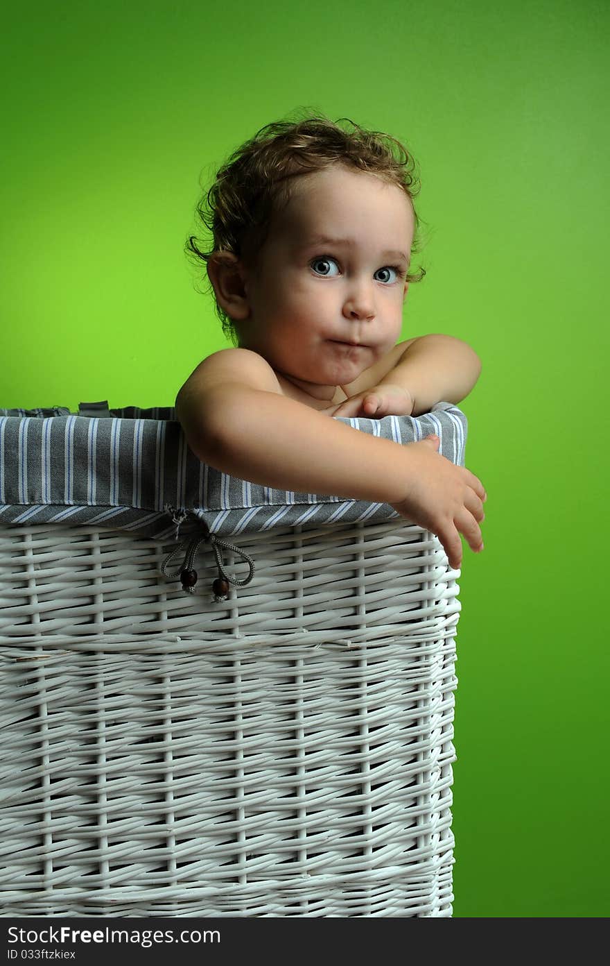 Baby sitting in a basket over a green background wall