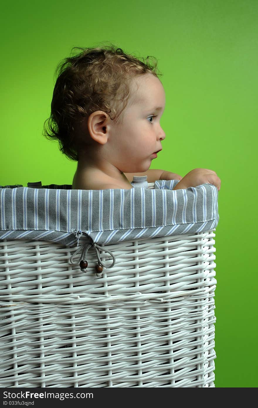 Baby sitting in a basket over a green background wall