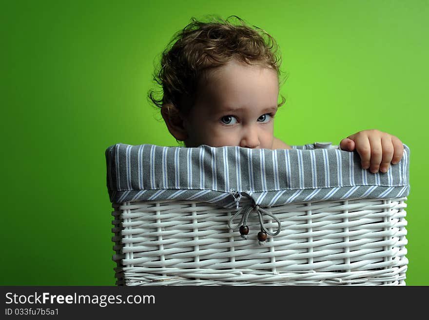 Baby sitting in a basket over a green background wall