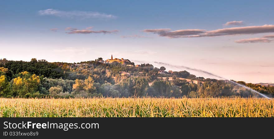 Watering a field of maize with Italian hill top village in background in early morning. Watering a field of maize with Italian hill top village in background in early morning