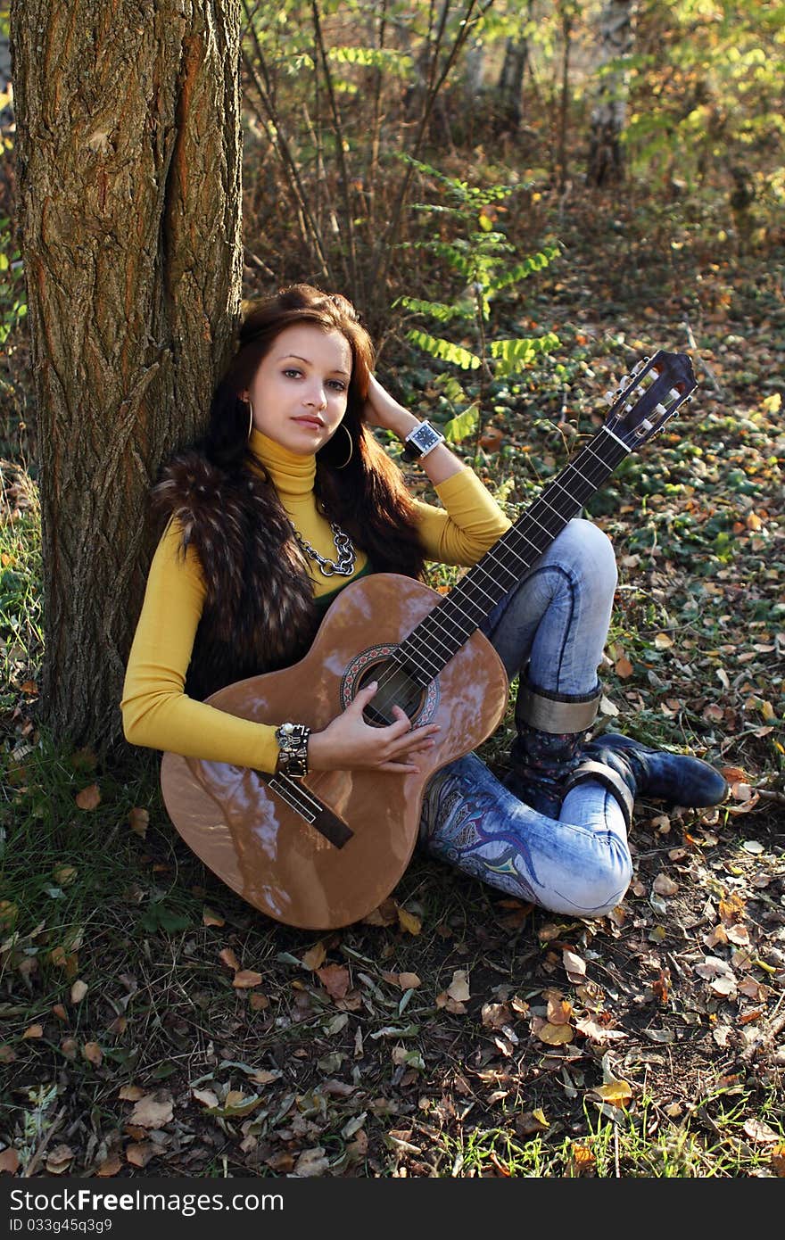 Beautiful brunette guitar player girl in the autumn forest