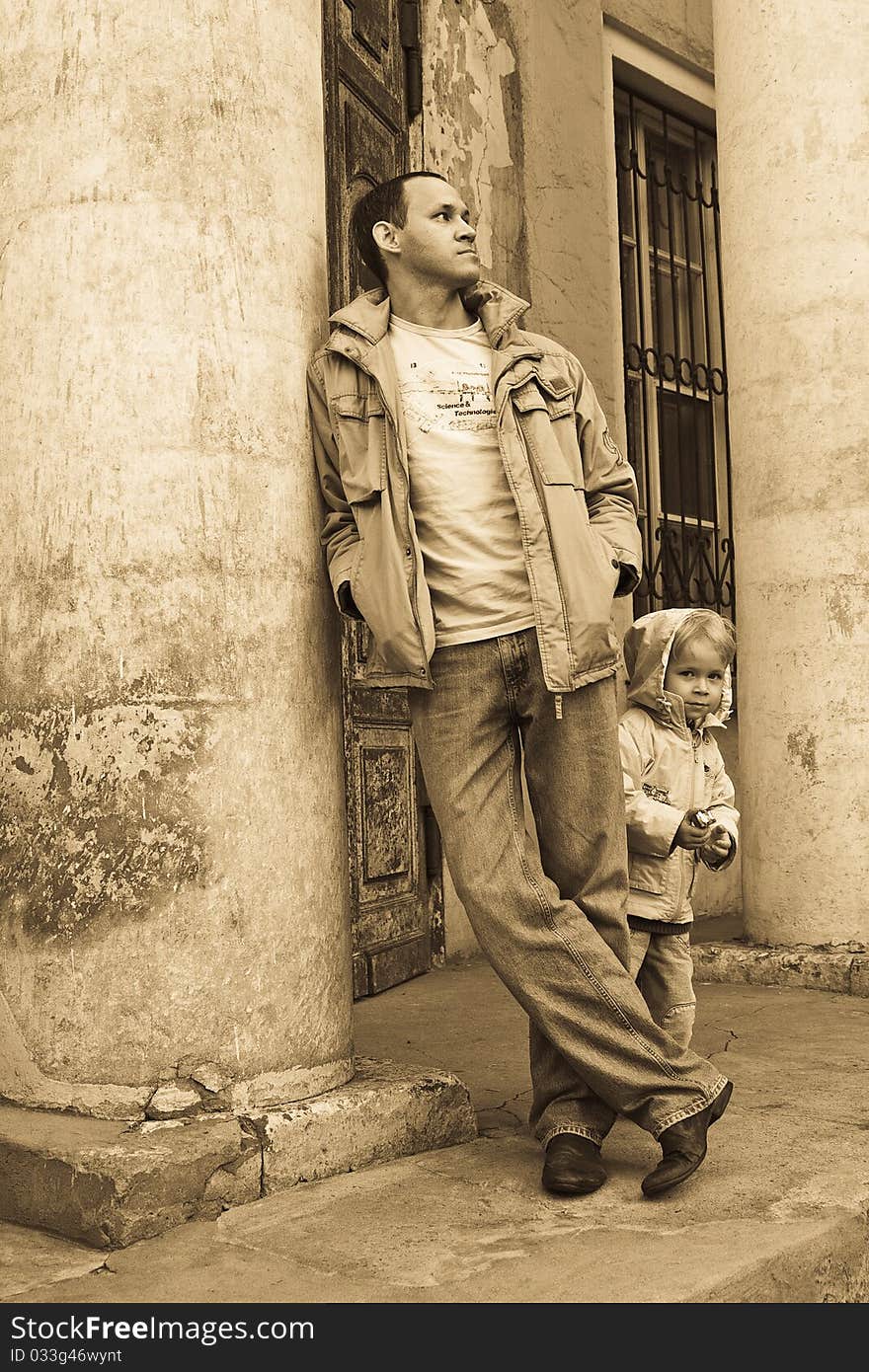 Man leaning against the column of a shabby building, child on the background. Man leaning against the column of a shabby building, child on the background