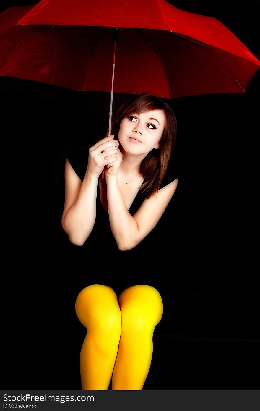 A woman holding a red umbrella and wearing yellow tights peeking out into the darkness. A woman holding a red umbrella and wearing yellow tights peeking out into the darkness.