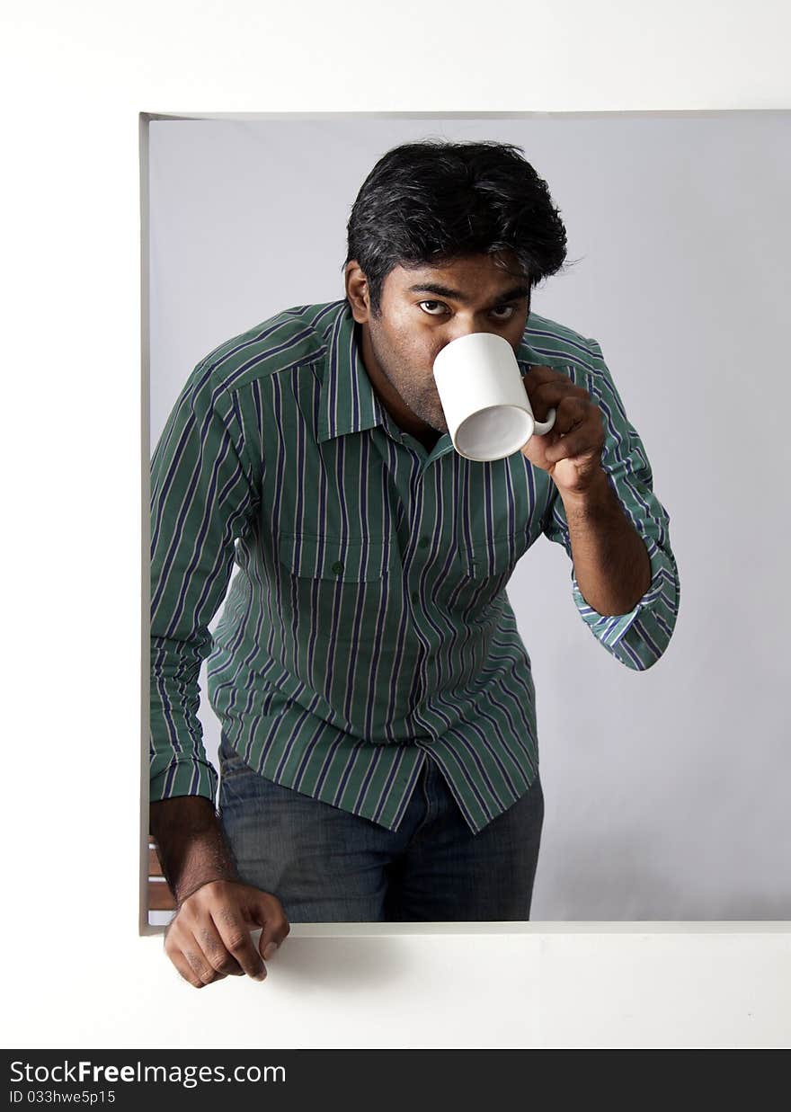 Young man having a beverage at an open window. Young man having a beverage at an open window