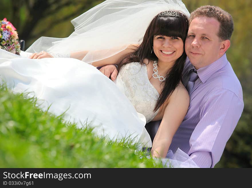 Happy groom and the bride sit on a grass