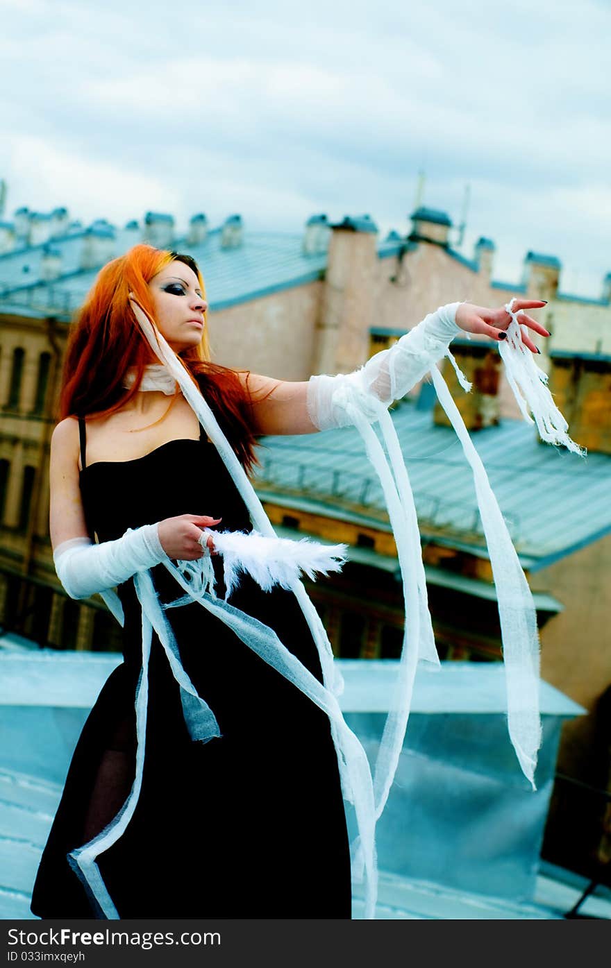 Photo of a Pretty red-haired girl with feathers, bandages and fan on rooftop