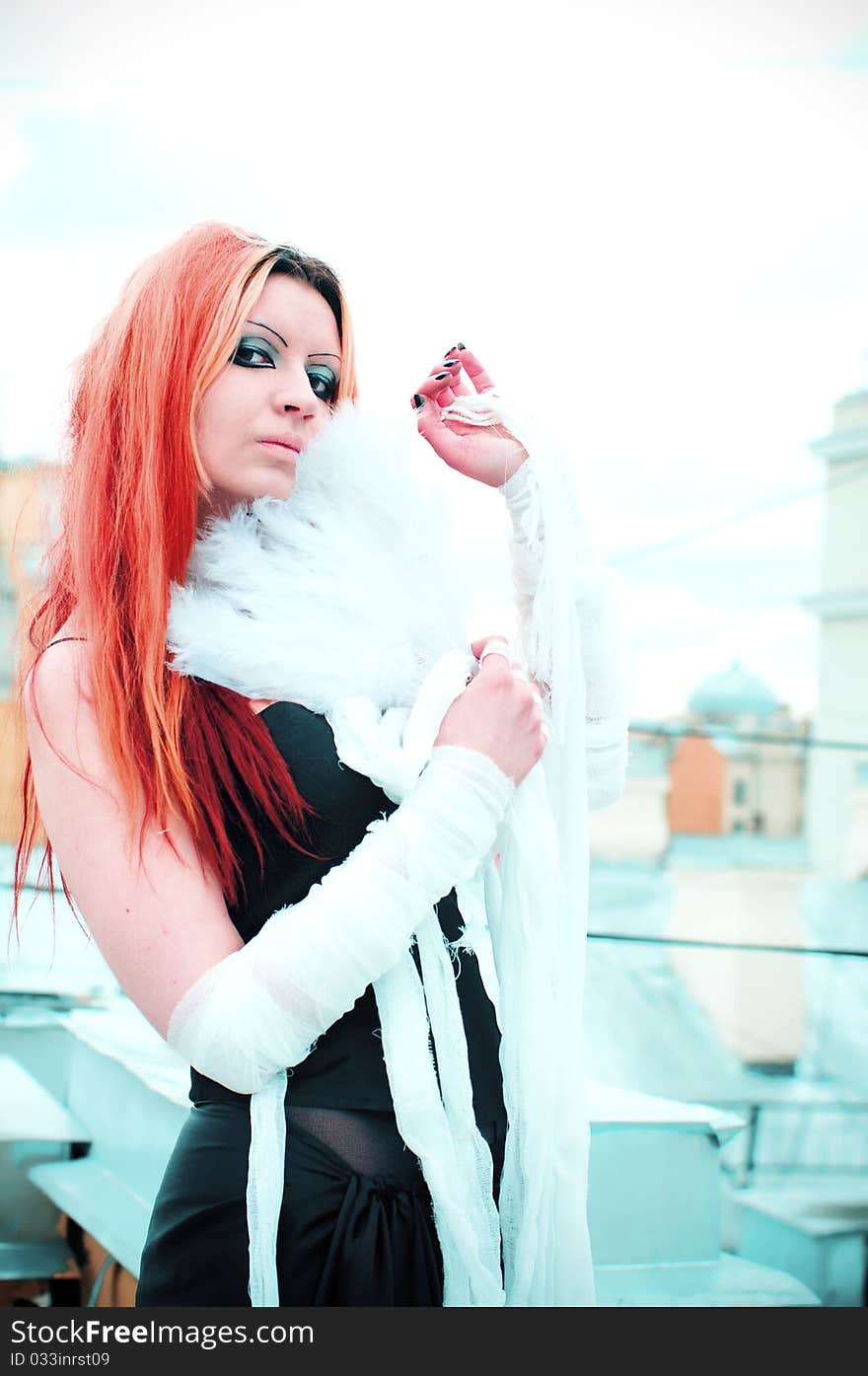 Photo of a Pretty red-haired girl with feathers, bandages and fan on rooftop