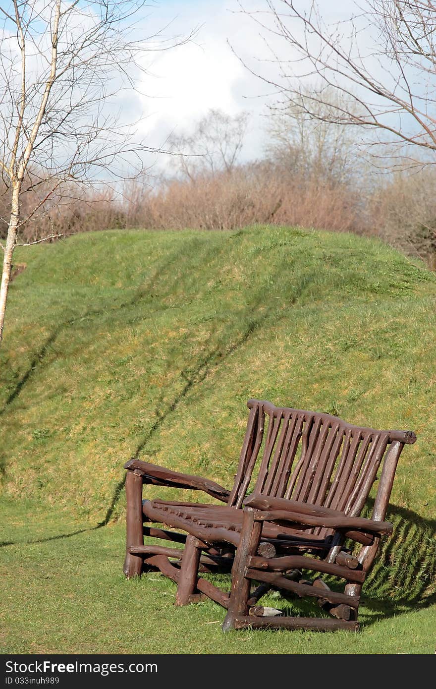 A solid wood park bench in grass surroundings