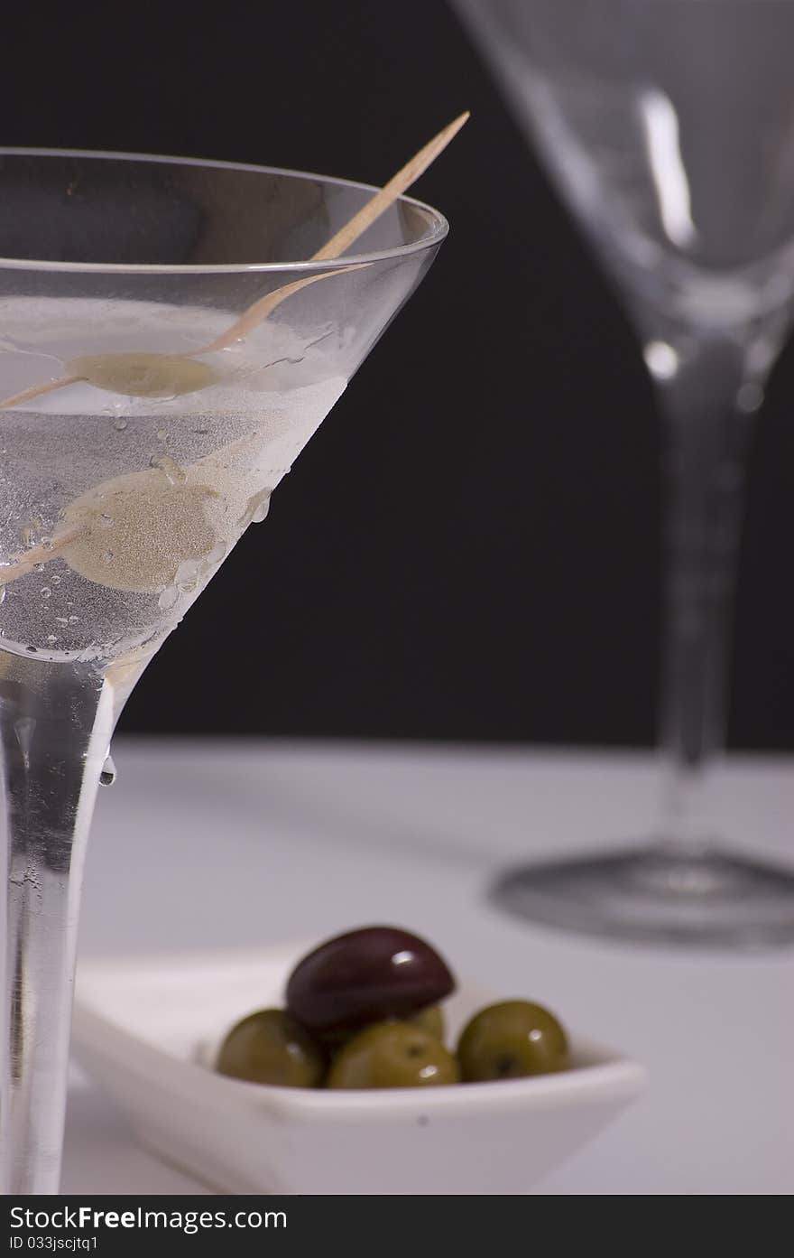 A glass of ice cold martini with olives and second glass in background. A glass of ice cold martini with olives and second glass in background