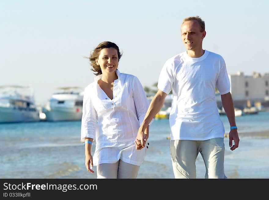 View of happy young couple walking on the beach, holding hands. View of happy young couple walking on the beach, holding hands.