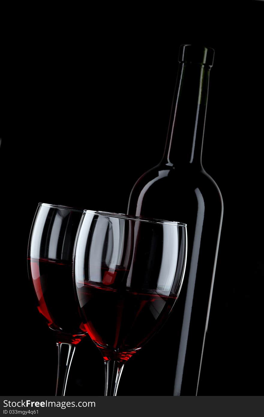 Bottle and glass of red wine on black background