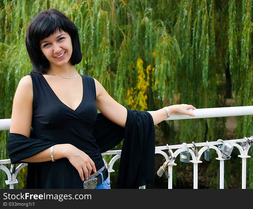 Smiling girl standing on the bridge on the background of green trees. Smiling girl standing on the bridge on the background of green trees