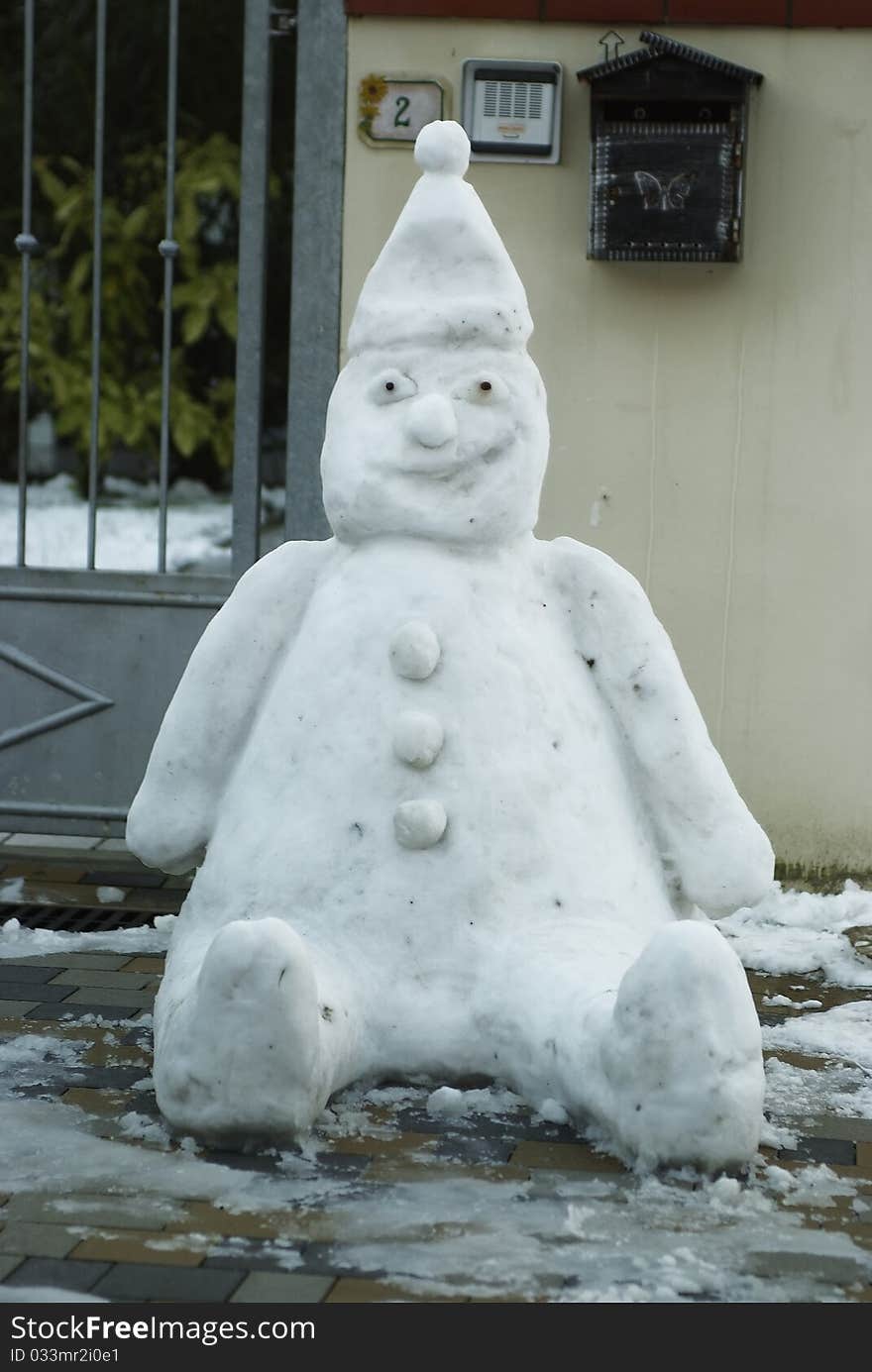 A little sitting snowman with snow cap