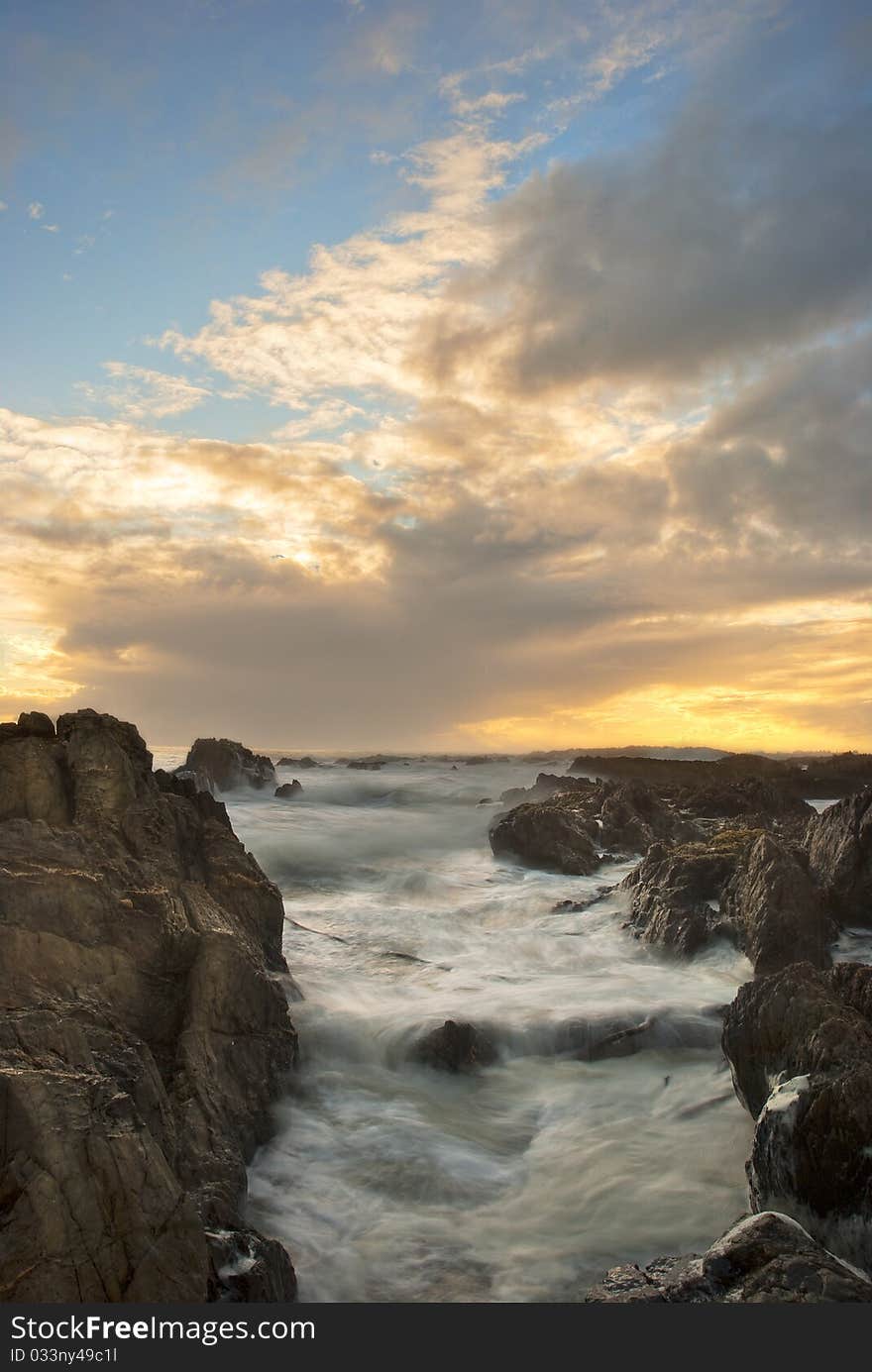 Sun setting over the ocean, with dramatic clouds overhead and rocks in the foreground. Sun setting over the ocean, with dramatic clouds overhead and rocks in the foreground