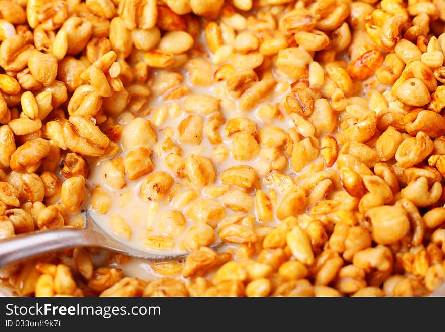 Granola with milk in glass bowl and spoon on white surface.