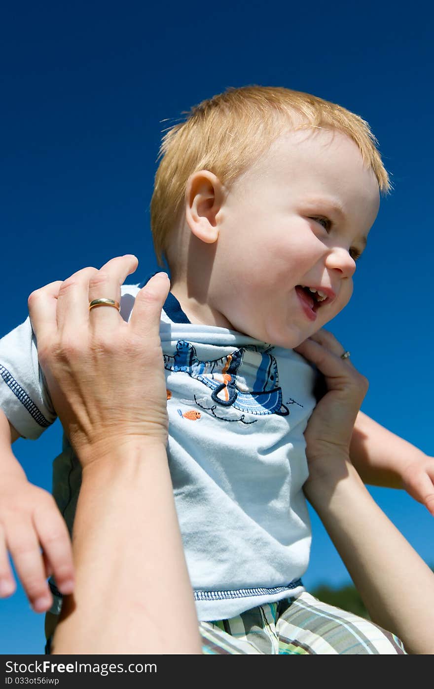 Laughing boy held up by his mother against blue sky. Laughing boy held up by his mother against blue sky