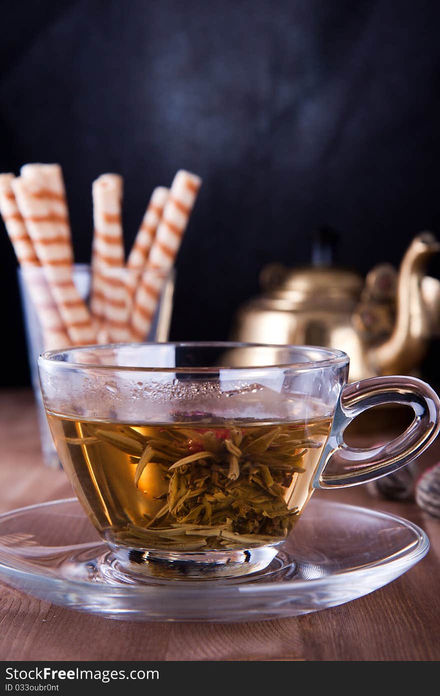 Transparent cup of a green tea with the sweet wafers and old teapot. Transparent cup of a green tea with the sweet wafers and old teapot