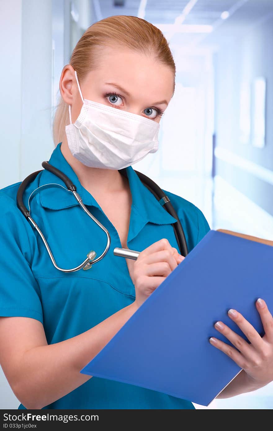 Young blond in medical gown with stethoscope and file folder in an hospital. Young blond in medical gown with stethoscope and file folder in an hospital