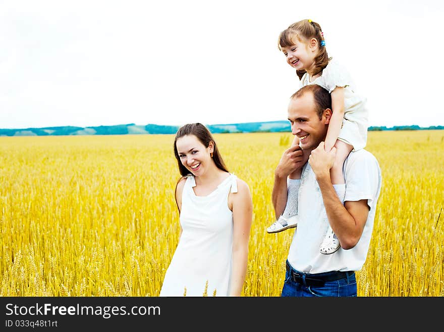 Happy family; young mother, father and their daughter having fun at the wheat field (focus on the child)