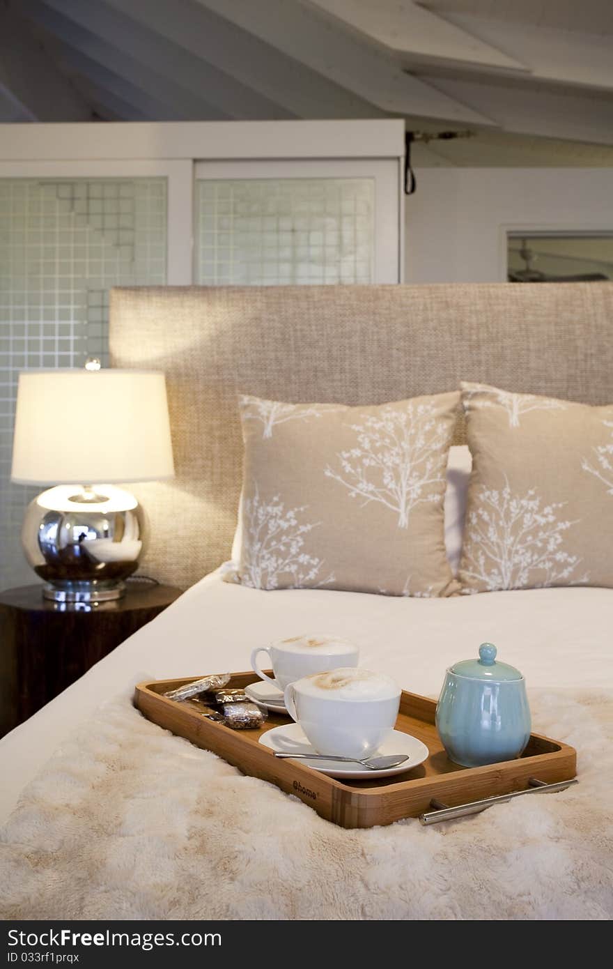 A tray of cappuccino coffee placed on a bed in a guest house. A tray of cappuccino coffee placed on a bed in a guest house