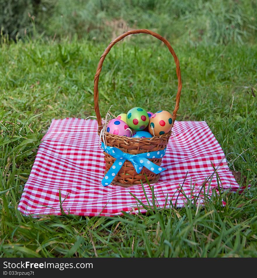 Colorful dotted easter eggs in a wicker basket on a green lawn