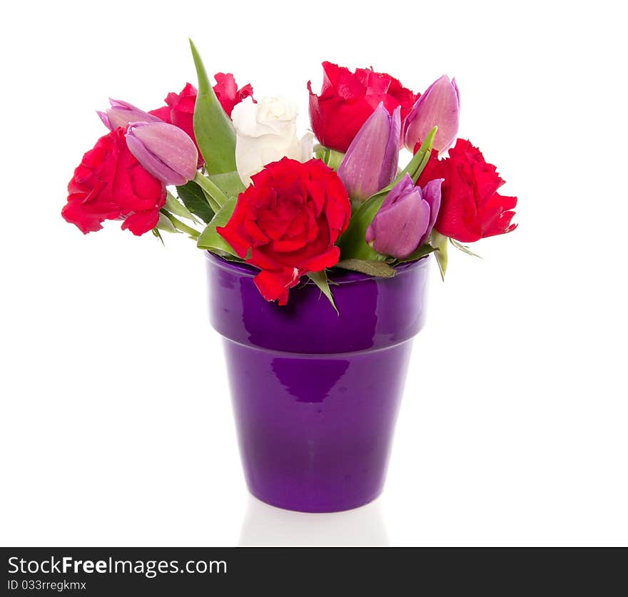 Red roses and purple tulips in a purple ceramic vase isolated over white