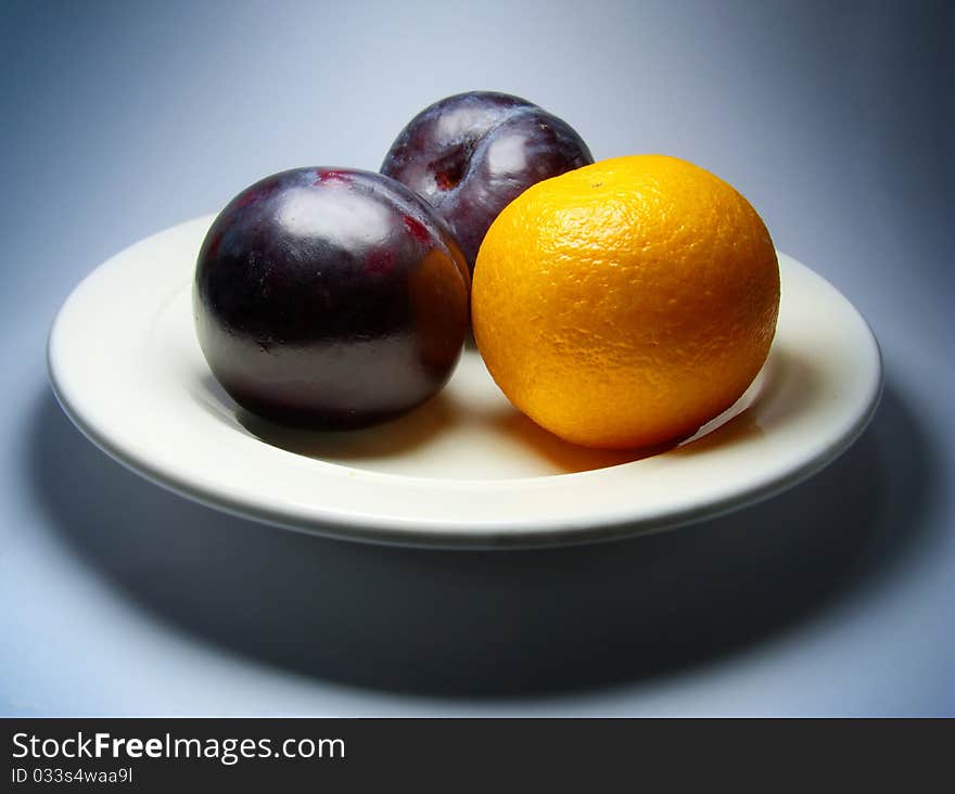 Plums and tangerine on plate. Dark blue background